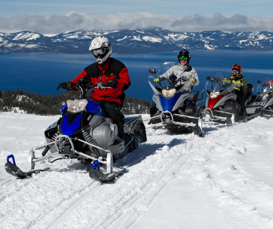 A group of people on snowmobiles with Lake Tahoe behind them.